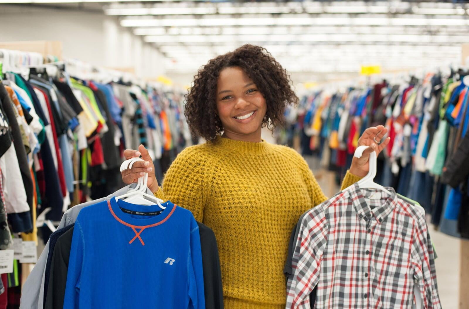 Beautiful mom holds two boys tops—one in each hand—as she shops the deals at her local sale.