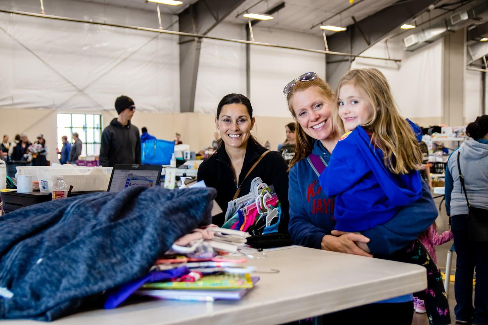 A mom and her daughter stand at the check out table with another mom.